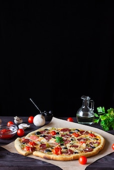 Pizza maison au salami, champignons et tomates cerises sur fond noir. vue de côté. espace libre pour le texte, photo verticale.