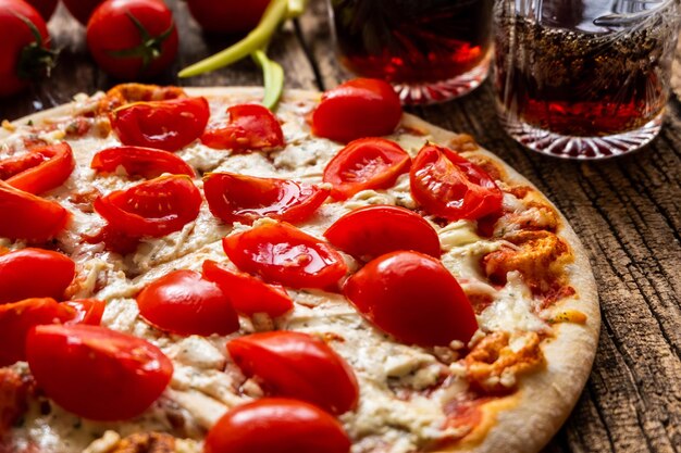 Une pizza Margarita avec du fromage et des tomates sur une planche de bois près de quelques verres avec des boissons