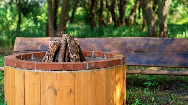 Place pour feu de camp avec banc en bois au glamping. Verdure autour