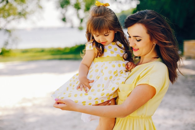 sur une plage ensoleillée avec du sable jaune, maman se promène dans une robe jaune et sa petite jolie fille