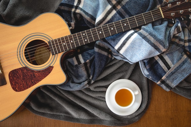 Plaids de guitare acoustique et une tasse de thé sur une vue de dessus de fond en bois