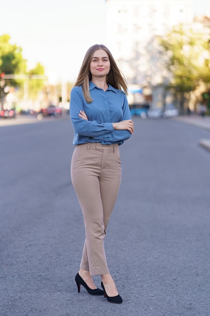 Photo gratuite plan d'une belle jeune femme d'affaires portant une chemise chifon bleue debout dans la rue, les bras croisés.