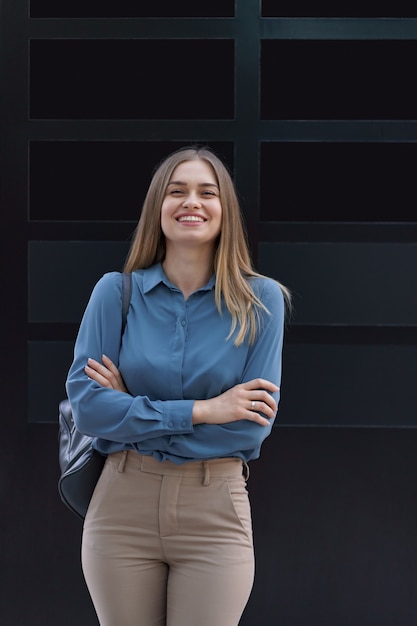 Photo gratuite plan de la belle jeune femme d'affaires portant une chemise en mousseline de soie bleue en position debout avec les bras croisés sur le mur noir