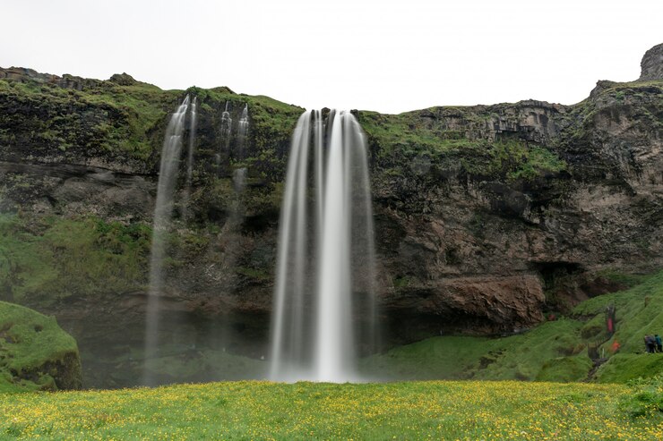 Photo gratuit plan d'une cascade qui coule sur un rocher au milieu d'un paysage verdoyant