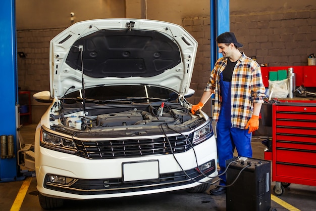 Photo gratuite plan complet d'un beau mécanicien automobile chargeant la batterie à l'aide de câbles métalliques dans une station-service moderne