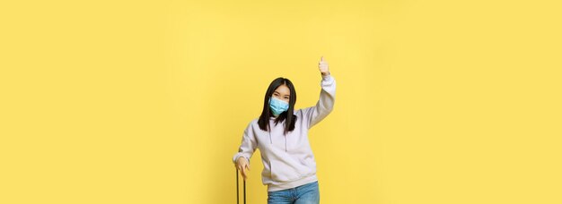 Plan complet d'une fille coréenne enthousiaste profitant de vacances posant avec une valise portant des médicaments pour le visage