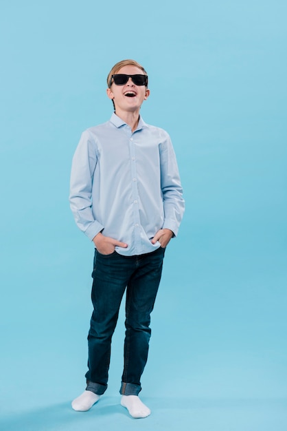 Plan complet d'un garçon moderne souriant posant avec des lunettes de soleil