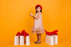 Photo gratuite plan complet d'une petite fille avec des sacs à provisions. mignon enfant en béret français rouge isolé sur mur jaune.