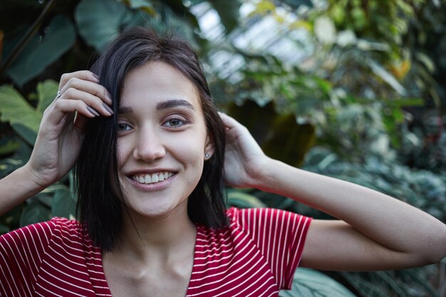 Plan extérieur d'une charmante étudiante joyeuse avec un sourire heureux, passant du temps libre dans un parc ou un jardin, se rechargeant après les cours au collège. Concept de personnes, nature, joie, repos et relaxation