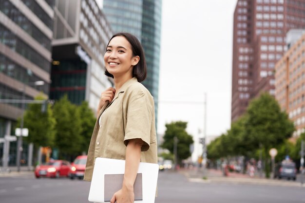 Plan extérieur d'une fille asiatique avec un ordinateur portable allant quelque part dans le centre-ville marchant dans la rue allant au travail