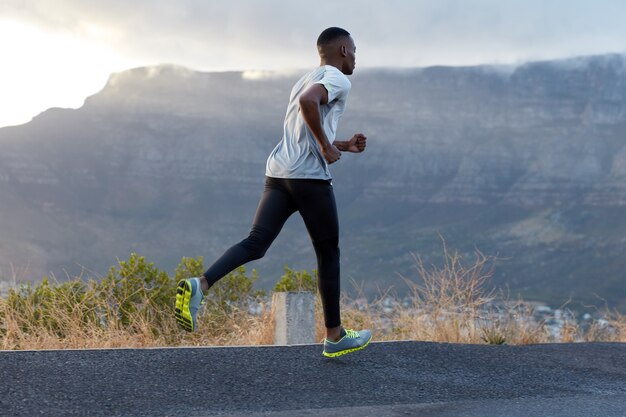 Plan extérieur d'un jeune homme athlétique portant un t-shirt décontracté, un pantalon et des baskets, pose contre la montagne, plein d'énergie, copie un espace pour votre contenu publicitaire ou votre promotion.