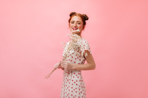 Plan d'une femme mignonne en robe midi et sandales à talons. Femme tenant des fleurs blanches sur fond rose.