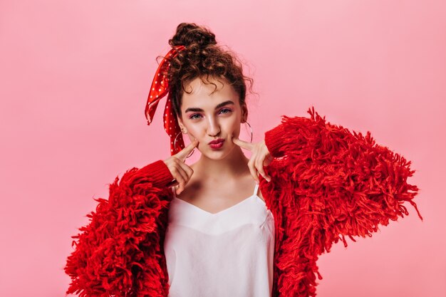 Plan d'une femme en veste de laine rouge se penche sur la caméra sur fond rose