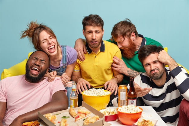 Plan horizontal d'amis drôles regarder une émission de télévision d'humour, exprimer différentes émotions, profiter d'un film de comédie