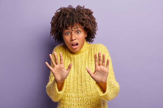 Photo gratuite plan horizontal d'une femme effrayée effrayée avec une coiffure afro, étend les paumes en geste de protection