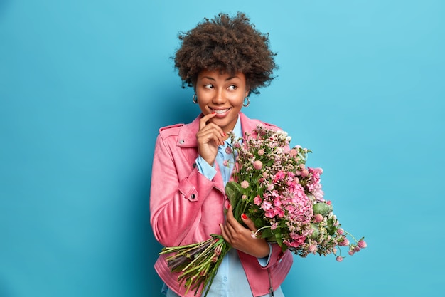 Plan horizontal d'une femme ethnique de rêve regarde joyeusement de côté hholds bouquet de fleurs