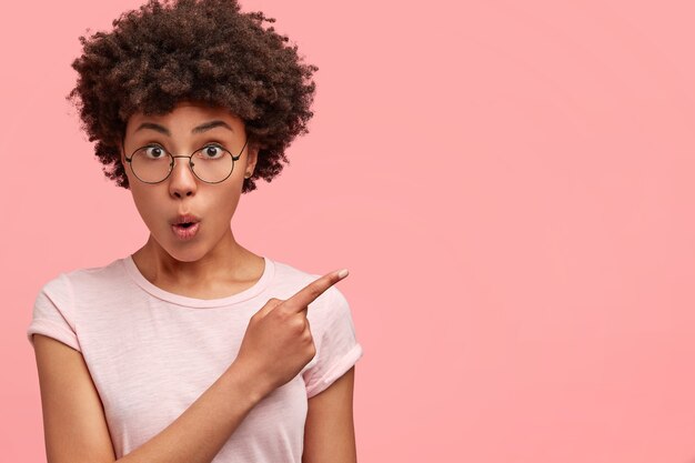 Plan horizontal d'une femme à la peau foncée choquée a les cheveux touffus et croustillants, pointe avec l'index