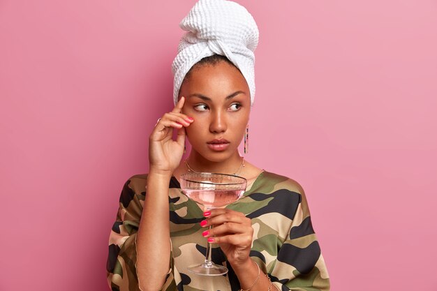 Plan horizontal d'une femme à la peau sombre réfléchie concentrée de côté pensivement a un teint bien soigné boit un cocktail