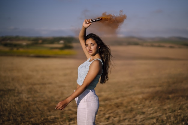 Plan horizontal d'une femme posant avec une bombe fumigène sur une distance de champs et de moulins à vent