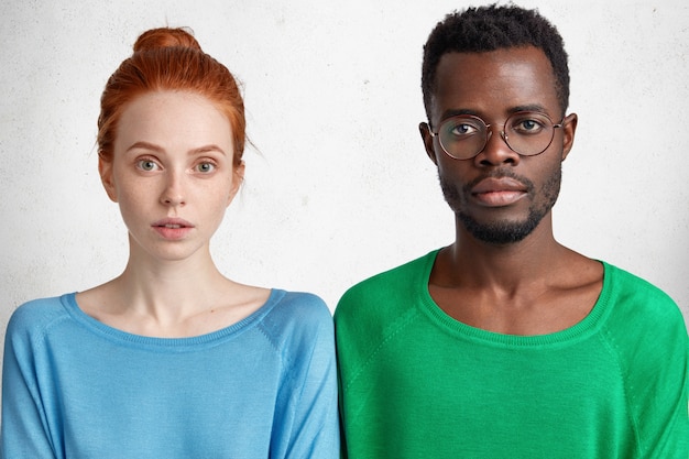 Photo gratuite plan horizontal d'une femme sérieuse au gingembre et de sa meilleure amie à la peau sombre à lunettes, se tiennent côte à côte