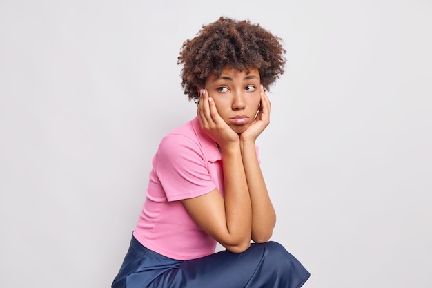 Photo gratuite plan horizontal d'une femme triste mécontente a une expression triste et réfléchie vêtue d'un t-shirt et d'une jupe se penche le visage sur les mains concentrées loin isolées sur un mur blanc