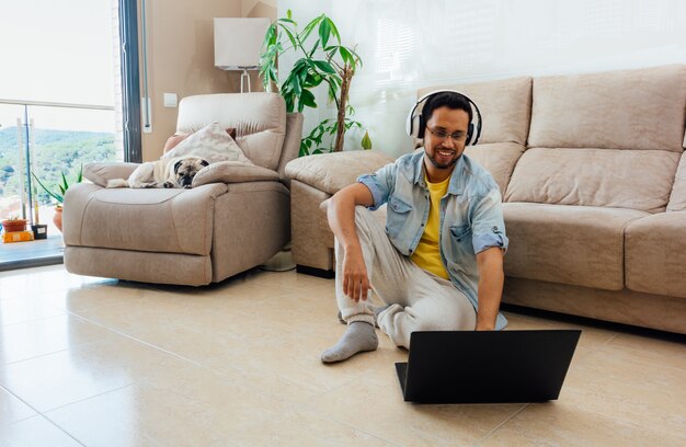 Plan horizontal d'un homme assis sur le sol, écouter de la musique et travailler avec un ordinateur portable à la maison