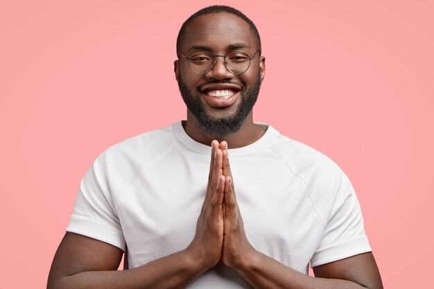 Plan horizontal d'un homme noir souriant maintient les mains jointes, croit en quelque chose de positif