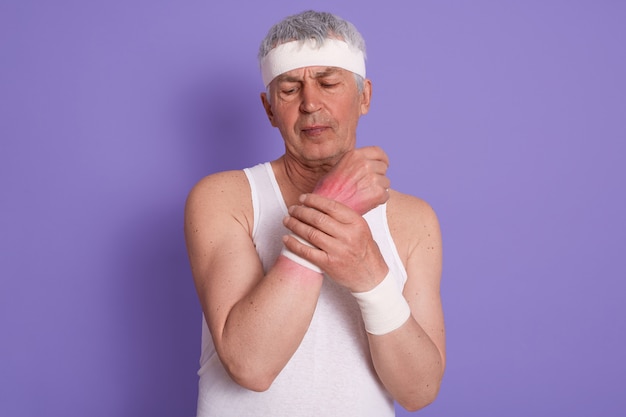 Plan horizontal d'un homme senior habille un t-shirt sans manches blanc, lui fait mal au poignet pendant l'entraînement sportif