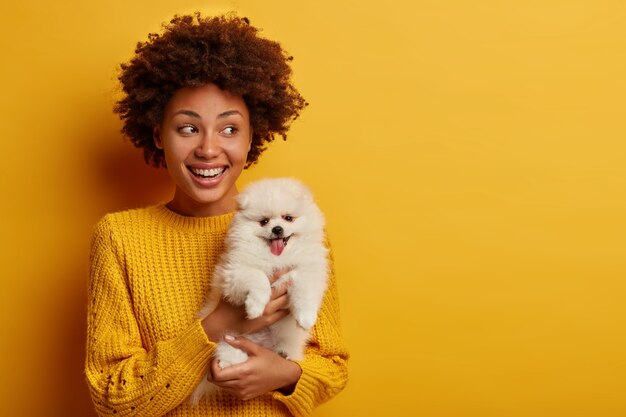 Plan horizontal d'hôtesse afro-américaine heureuse pose avec mignon chiot spitz