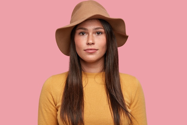 Plan horizontal de la jeune femme avec une apparence attrayante, peau tachetée de rousseur, regarde sérieusement la caméra