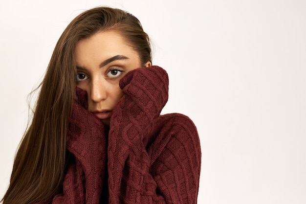 Plan Horizontal D'une Jeune Femme Caucasienne Malheureuse Sérieuse Portant Un Pull En Tricot à Manches Longues, Essayant De Se Réchauffer Par Une Froide Journée D'hiver Venteuse, Tenant Les Mains Sur Ses Joues.