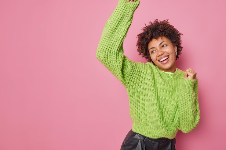 Photo gratuit plan horizontal d'une jeune femme heureuse dansant des mouvements insouciants lève activement les bras sourit largement porte un pull tricoté vert concentré isolé sur fond rose avec espace de copie