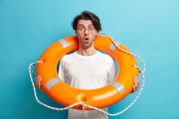 Photo gratuite plan horizontal d'un jeune homme choqué secouriste de plage pose bouée gonflée garde la bouche ouverte