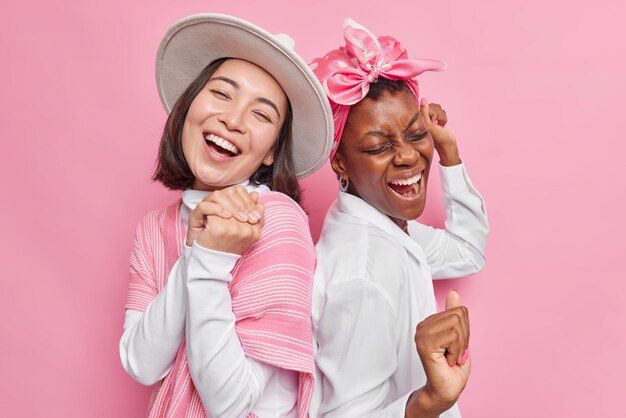 Plan horizontal de jeunes modèles féminins joyeux s'amuser ensemble danser avec le rythme de la musique rire se tenir joyeusement les uns aux autres isolés sur fond rose idiot autour. Notion de bonheur.