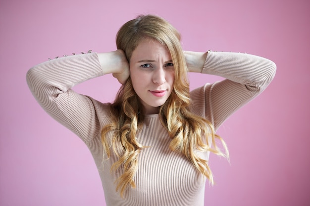 Plan horizontal d'une jolie jeune femme stressée fronçant les sourcils, couvrant les oreilles des deux mains, ne supportant pas le bruit terrible et insupportable provenant du voisin qui écoute de la musique trop fort dans son appartement