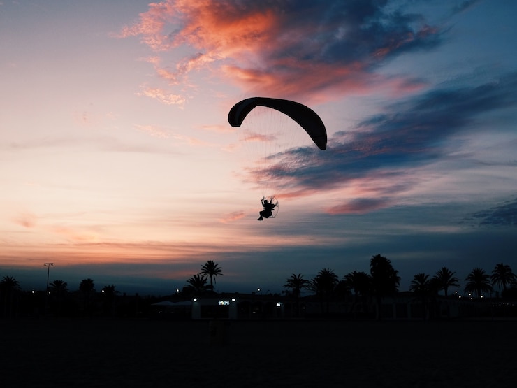 Photo gratuit plan horizontal d'une plage avec une personne glissant sur un parachute de paramoteur