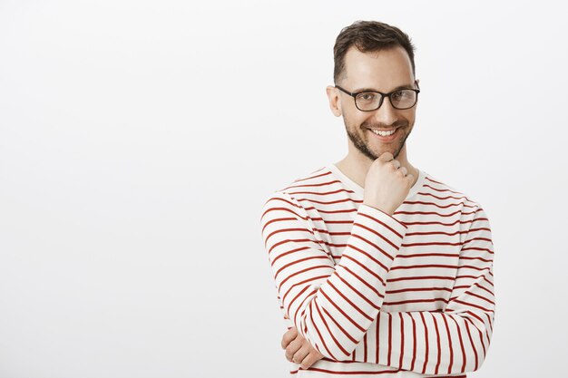 Plan intérieur d'un bel homme ludique à lunettes noires, souriant avec une expression intriguée, ayant un désir ou une intension intéressante