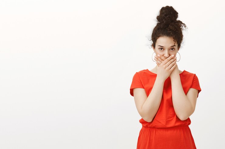 Photo gratuit plan intérieur d'une belle femme urbaine dégoûtée intense en robe rouge, croisant les paumes sur la bouche et regardant fixement