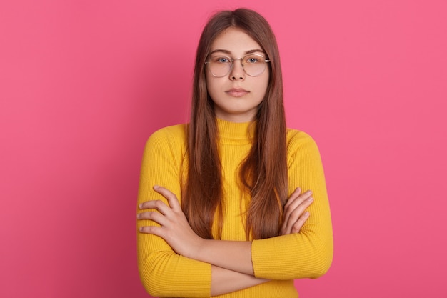 Plan intérieur d'une femme sérieuse ou en colère, les bras croisés. Jeune fille aux cheveux longs robes chemise jaune