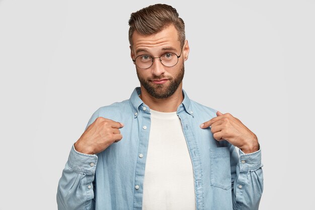 Plan intérieur d'un homme barbu sérieux posant contre le mur blanc