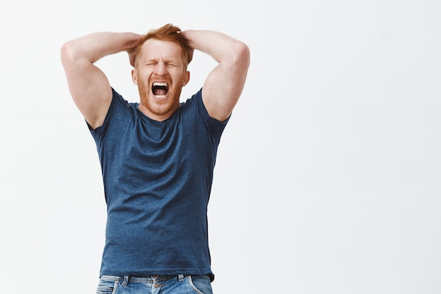 Plan intérieur d'un homme rousse ressentant de la détresse et des émotions douloureuses, se tenant les mains sur la tête, criant ou hurlant les yeux fermés