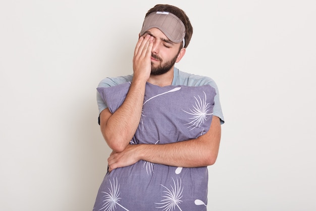 Plan intérieur d'un jeune homme séduisant se réveiller le matin, veut dormir, beau mec qui s'étend et bâille, tenant ses pilos