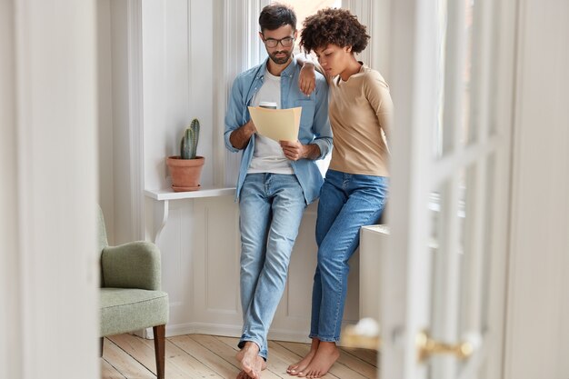 Plan intérieur de propriétaires d'entreprise se tenant l'un près de l'autre, étudiant la documentation, tenant une tasse de café