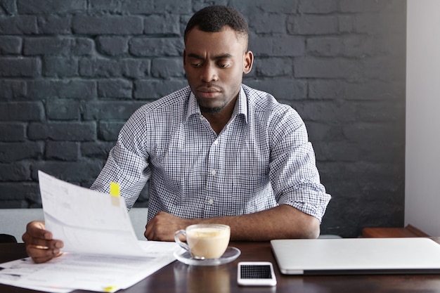 Plan intérieur d'un sérieux financier afro-américain étudiant des documents financiers pendant la pause-café au café