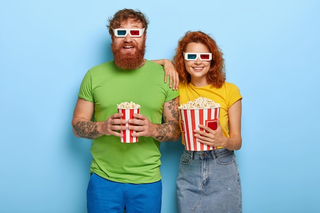 Plan Isolé D'une Femme Heureuse Au Gingembre Et De Son Mari Barbu Viennent Au Cinéma Le Soir, Ont Des Visages Et Des Sourires Heureux, Portent Des Lunettes En Trois Dimensions, Mangent Une Délicieuse Collation En Regardant Un Film