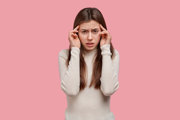 Plan d'une jeune femme triste garde les doigts sur les tempes, a mal à la tête, se sent épuisée et mécontente, essaie de penser à résoudre le problème