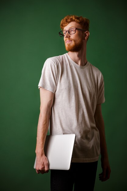 Plan d'un jeune hipster à tête de lecture barbu, tenant un ordinateur portable, détournant les yeux