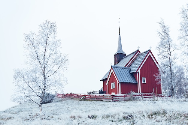 Plan large d'un bâtiment rouge dans une zone enneigée entourée d'arbres nus couverts de neige sous un ciel clair