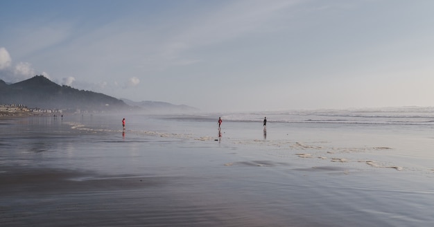 Plan large d'enfants jouant au bord de la mer sous un ciel bleu nuageux