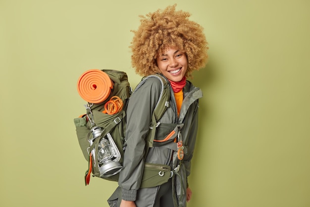 Photo gratuite plan latéral d'une randonneuse joyeuse vêtue d'une veste portant un sac à dos avec l'équipement nécessaire menant à un mode de vie sain et actif isolé sur fond vert concept de voyage et de vacances